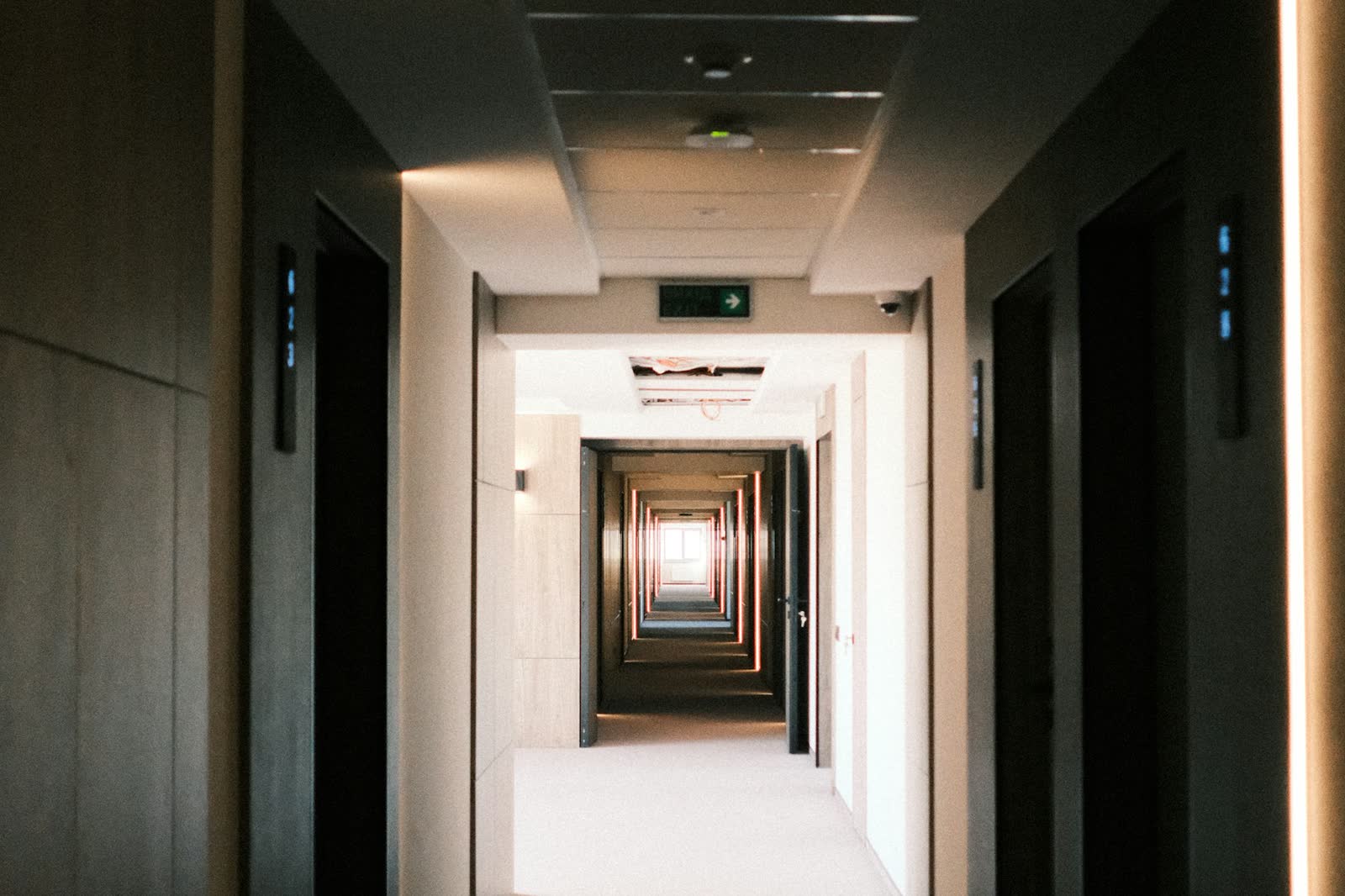 A long, dimly lit hotel corridor with a row of doorways receding into the distance, creating a strong vanishing-point perspective.